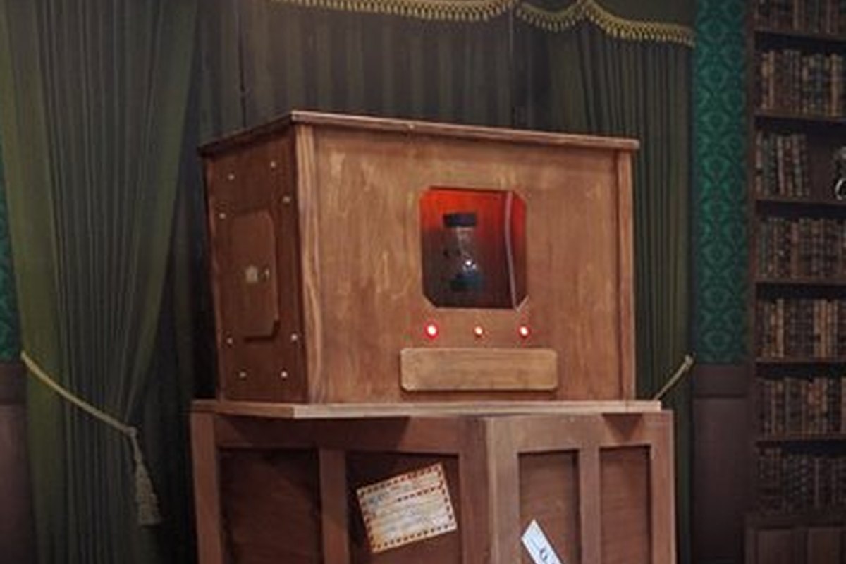 Gros plan sur le colis piégé de l'escape game mobile Sherlock Holmes, coffre de bois à façade rouge, sablier et voyants du compte à rebours