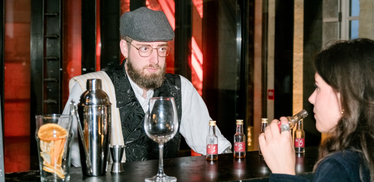 Un comédien en costume de barman sert deux participantes au bar du gala