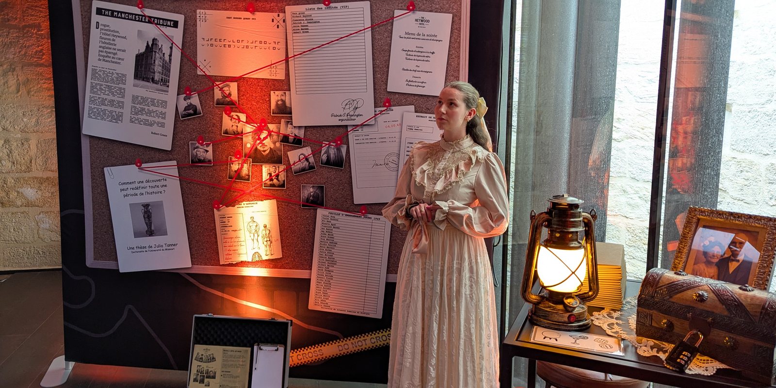 Comédienne en costume Belle Époque devant le tableau d'enquête Murder Quest, mallette de détective et lanterne