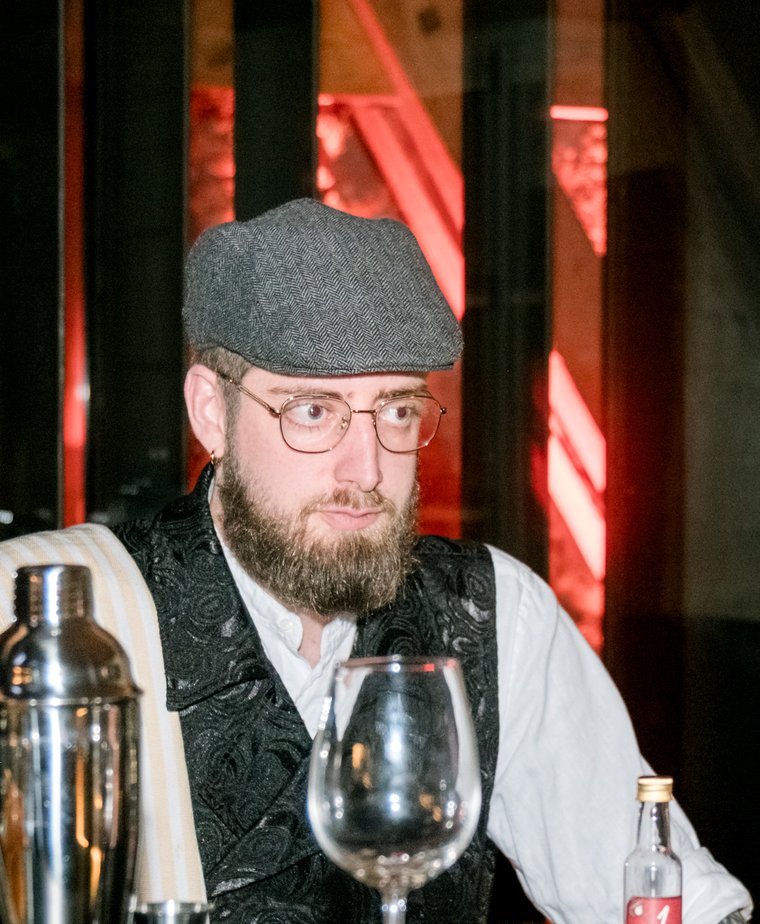 Le Barman, un des convives suspects du gala, casquette et gilet, derrière son comptoir