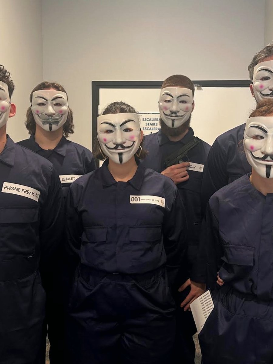 Six participants masqués avec badges de code, en combinaison bleu marine