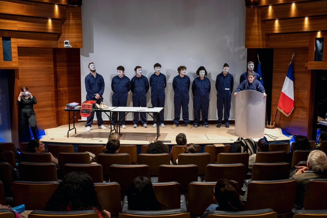 Grand groupe de participants masqués alignés sur scène devant un auditorium