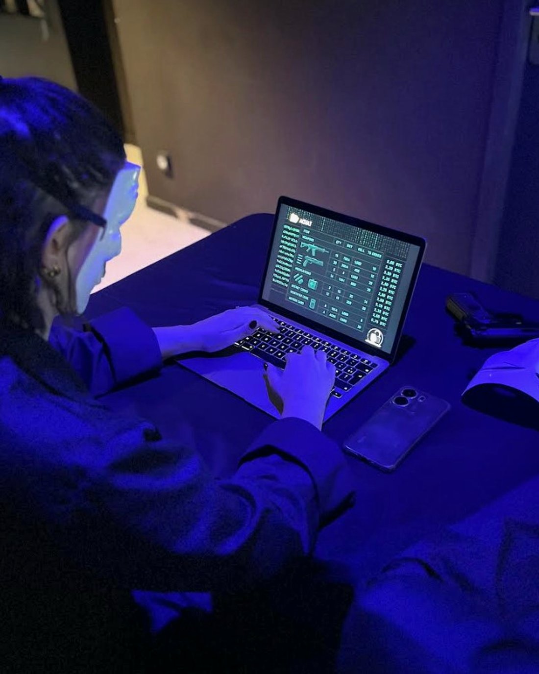 Joueuse masquée infiltrant un système sur ordinateur portable, écran terminal vert sous lumière bleue