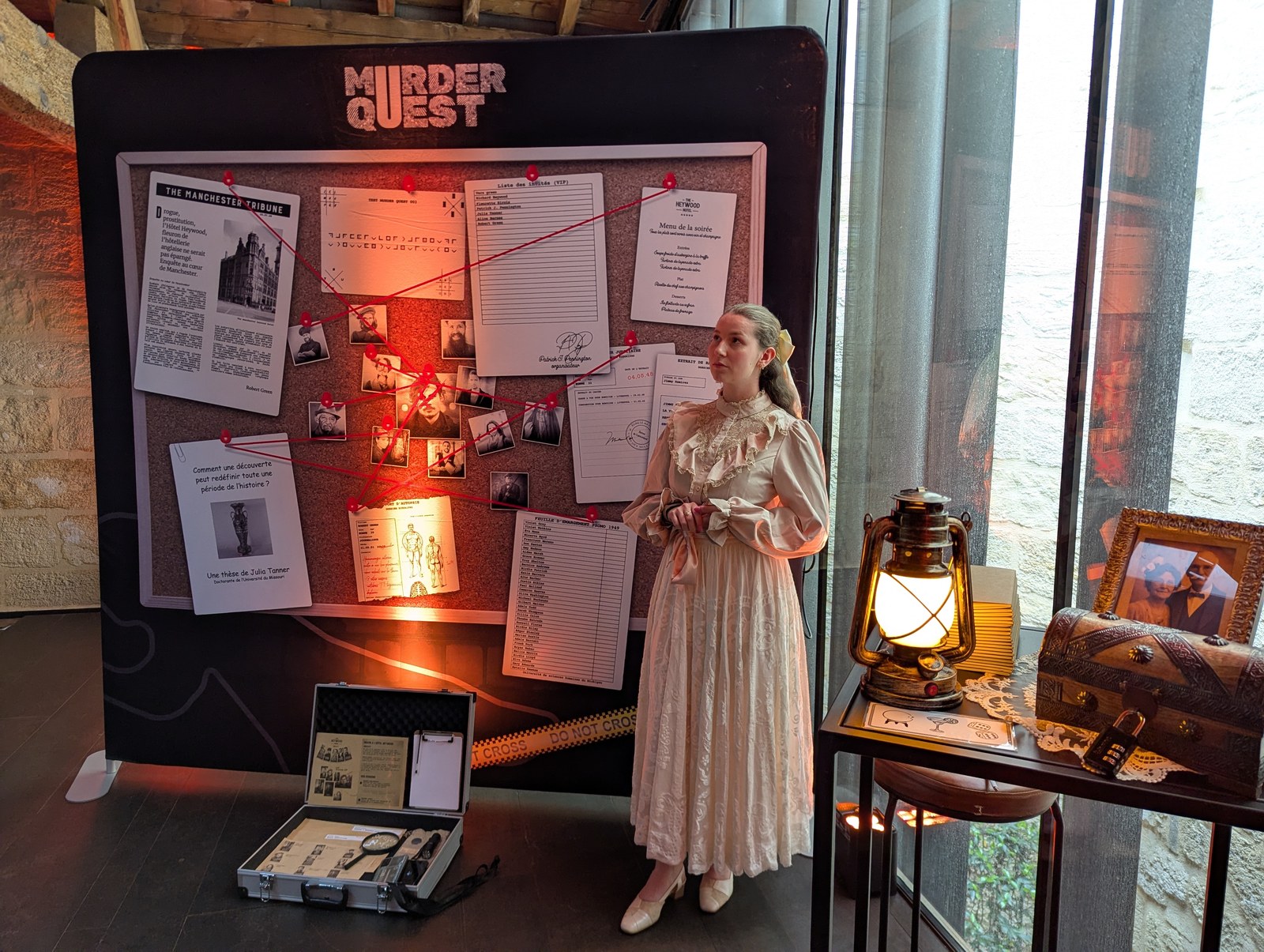 Le vrai tableau d'enquête Murder Quest en conditions réelles, une comédienne en costume d'époque se tient à côté, indices reliés par un fil rouge