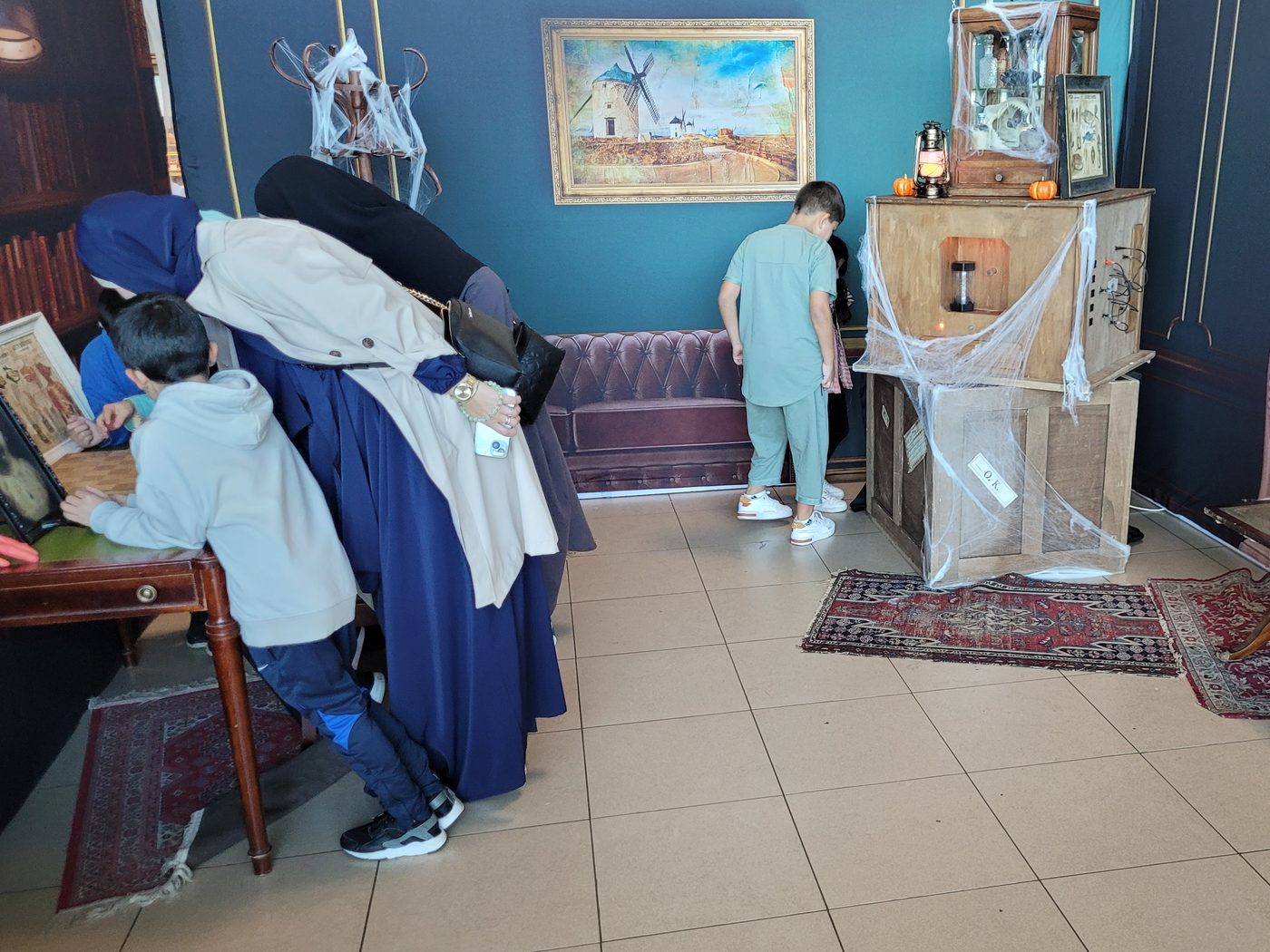Enfants et parents fouillent un décor d'Halloween garni de toiles d'araignée et de citrouilles pendant un escape game mobile