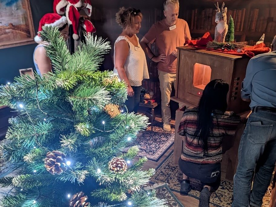 Adultes en pleine partie dans le décor de L'Atelier du Père Noël, sapin illuminé au premier plan